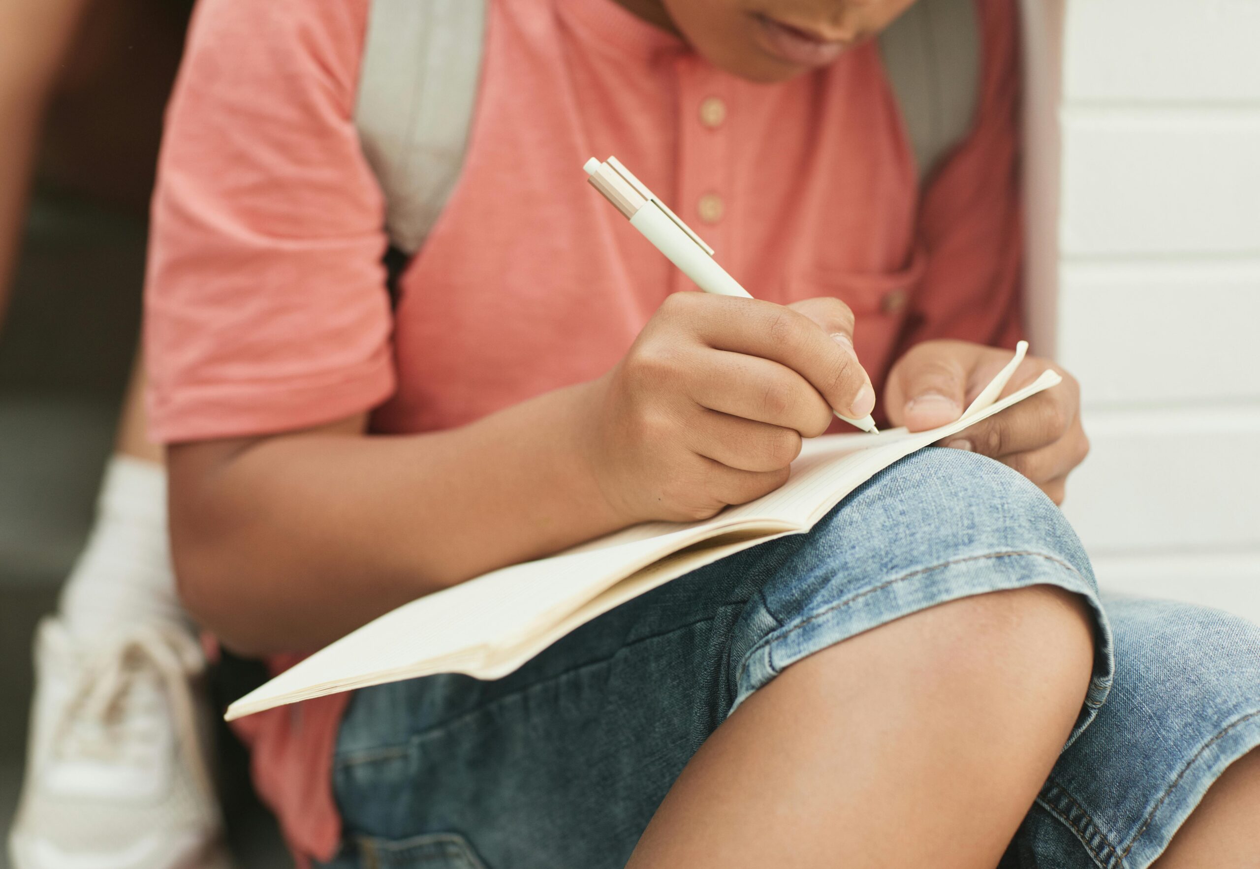 A teenager sitting outside writing in a notebook, symbolizing summer education and creativity.